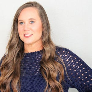 May include: A woman with long brown hair wearing a navy blue crocheted sweater.