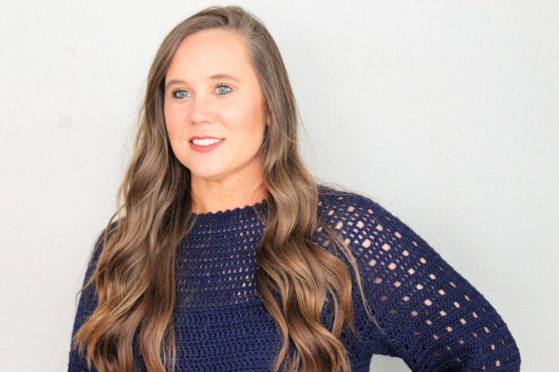May include: A woman with long brown hair wearing a navy blue crocheted sweater.