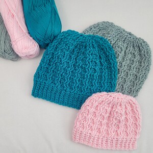 May include: Three crocheted hats in different colors: teal, gray, and pink. The hats are made with a textured stitch pattern.