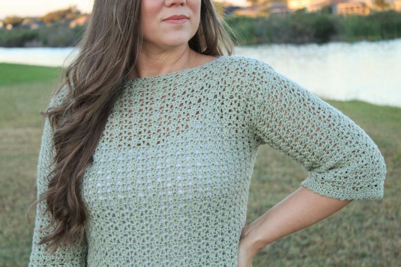 May include: A light green crochet sweater with three-quarter sleeves. The open weave design is visible, and the sweater has a boat neck. The garment is made of a soft, textured yarn.
