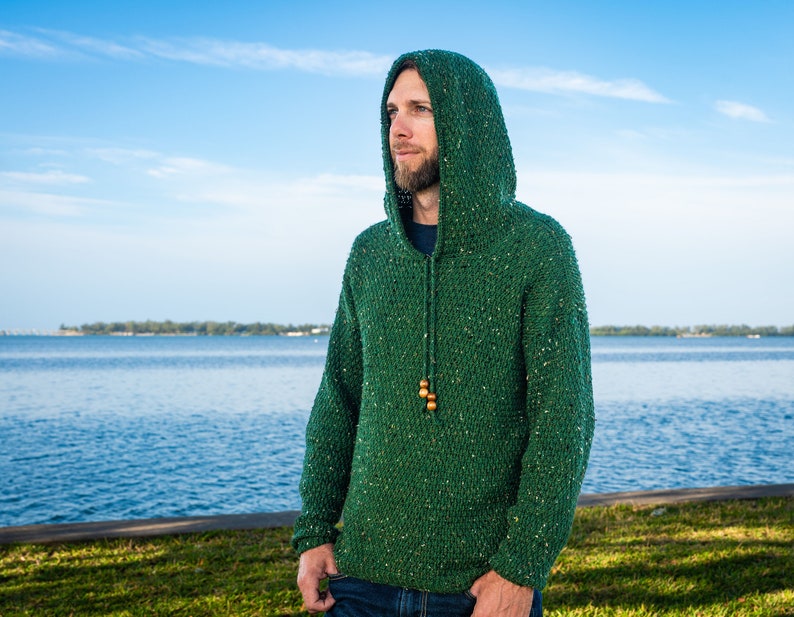 May include: A green hooded sweater with a speckled texture. The sweater has a drawstring with wooden beads.