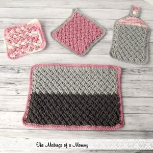 Puede incluir: Una colecci&oacute;n de art&iacute;culos de cocina de ganchillo hechos a mano en tonos rosa, gris y blanco. El conjunto incluye un salvamanteles cuadrado, un pa&ntilde;o de cocina, una toalla para colgar y una alfombra rectangular. Los art&iacute;culos est&aacute;n dispuestos sobre una superficie de madera clara.