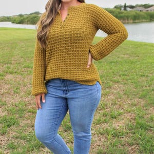 May include: A woman wearing a mustard yellow waffle knit sweater with a button closure at the neck and blue jeans.