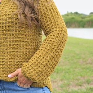 May include: A mustard yellow waffle knit sweater with long sleeves. The sweater has a button-up collar and is made of a soft, comfortable fabric.