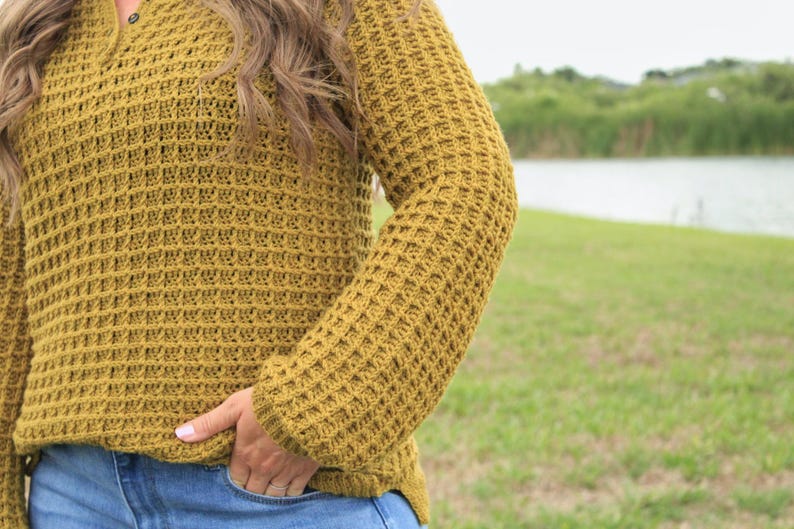 May include: A mustard yellow waffle knit sweater with long sleeves. The sweater has a button-up collar and is made of a soft, comfortable fabric.
