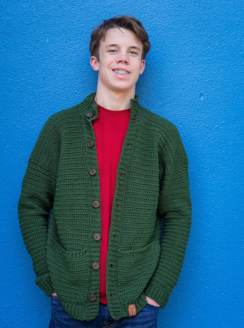 May include: A green crocheted cardigan with a red t-shirt underneath. The cardigan has a button closure and two pockets.