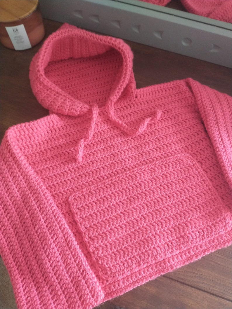May include: A pink crocheted hooded sweater with a pocket on the front.