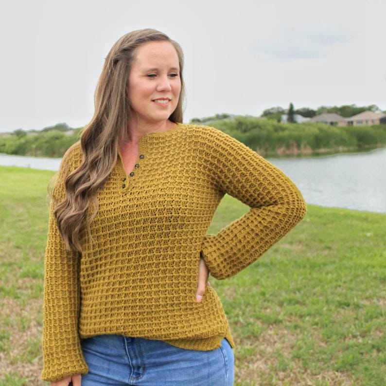 May include: A mustard yellow waffle knit sweater with a button-up neckline. The sweater has long sleeves and a relaxed fit.