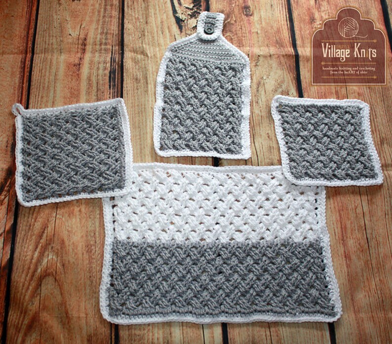 Puede incluir: Un juego de cocina de ganchillo hecho a mano en gris y blanco. El juego incluye un pa&ntilde;o de cocina, dos agarraderas y una alfombra rectangular. Los art&iacute;culos tienen un patr&oacute;n texturizado y ribete blanco. El logotipo de Village Knits est&aacute; en la esquina superior derecha.