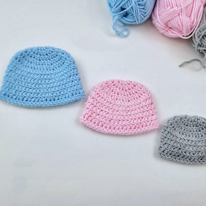 May include: Three crocheted hats in different colors: light blue, pink, and gray. The hats are made with a simple stitch pattern and are all the same size.