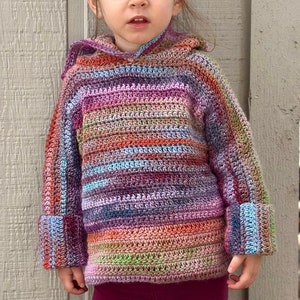 May include: A young child wearing a colorful striped crocheted hooded sweater with long sleeves and burgundy leggings.