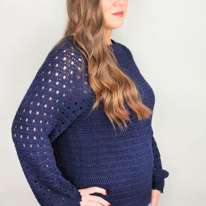 May include: A navy blue crocheted sweater with a lacy pattern on the sleeves. The sweater has a relaxed fit and a round neckline.