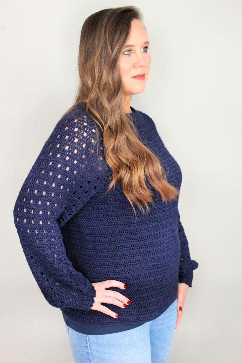 May include: A navy blue crocheted sweater with a lacy pattern on the sleeves. The sweater has a relaxed fit and a round neckline.