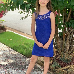 May include: A young person wearing a blue crocheted sleeveless dress with a white crocheted neckline. The dress is knee-length and has a simple, elegant design.
