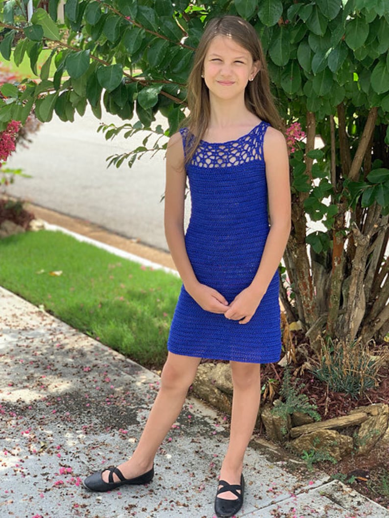 May include: A young person wearing a blue crocheted sleeveless dress with a white crocheted neckline. The dress is knee-length and has a simple, elegant design.