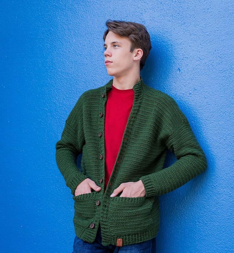 May include: A green crocheted cardigan with a red t-shirt underneath. The cardigan has a button-up front and two pockets.