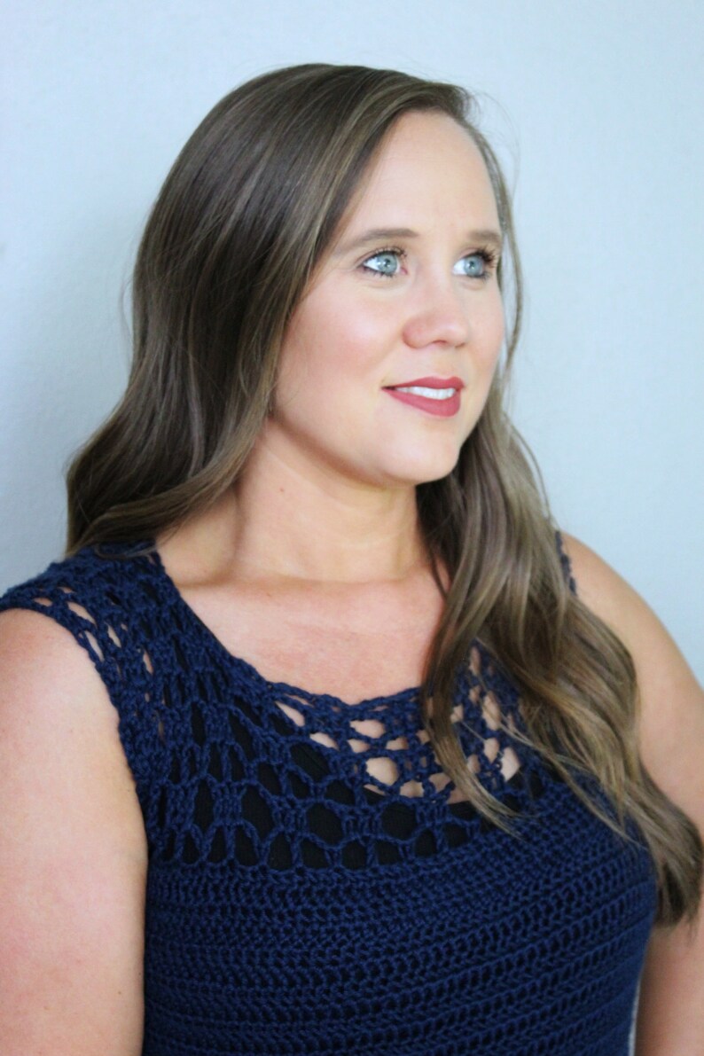May include: A woman wearing a navy blue crochet top with a delicate openwork pattern. The top has a scoop neckline and sleeveless design.