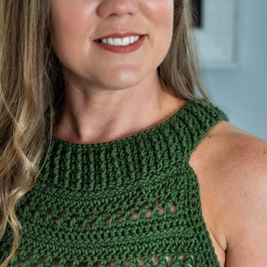 May include: A green crochet top with a high neckline and openwork design. The top is sleeveless and appears to be handmade. The colour is a deep, forest green.