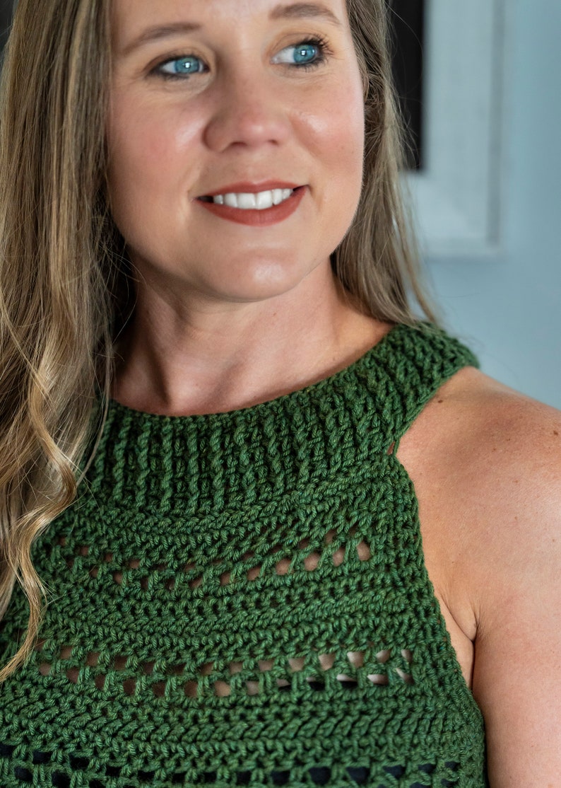 May include: A green crochet top with a high neckline and openwork design. The top is sleeveless and appears to be handmade. The colour is a deep, forest green.