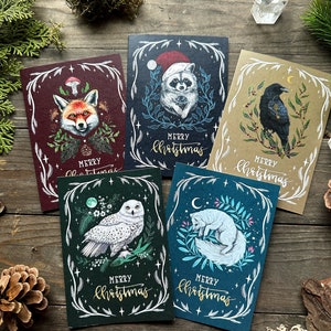 Może przedstawiać: Pięć kartek świątecznych z ilustracjami zwierząt leśnych: lisa, szopa, kruka, sowy i lisa polarnego. Każda kartka ma unikalną ilustrację z napisem "Merry Christmas".
