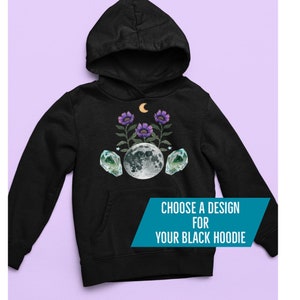 May include: Black hoodie with a celestial design. It features a full moon, purple flowers, green crystals, and a crescent moon. The text "CHOOSE A DESIGN FOR YOUR BLACK HOODIE" is on a teal banner.