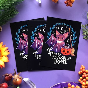 May include: Three black cards with a purple bat holding a pumpkin bucket and a broom. The card on the right says "Trick or Treat" in white cursive lettering.