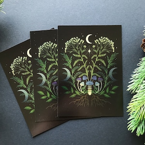 May include: Three black cards with a dark green, white, and blue floral design. The design features a symmetrical arrangement of flowers, leaves, and mushrooms with crescent moons in the background.