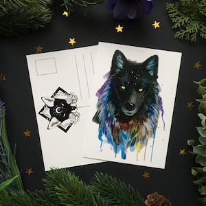 Puede incluir: Dos postales blancas con arte de lobos. Una presenta un lobo negro con un diseño de cielo estrellado y detalles de acuarela. La otra tiene un diseño de lobo en blanco y negro con un borde de diamante. El fondo es negro con estrellas doradas y vegetación.