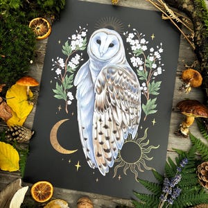 May include: A black and gold print featuring a white barn owl with a halo of gold stars and a crescent moon. The owl is surrounded by white flowers and green leaves. The print is on a black background.