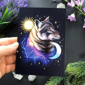 Puede incluir: Un lobo aullando a la luna con una constelación de estrellas detrás. El lobo es gris y blanco con una galaxia azul y morada detrás. La luna es una media luna y es azul y blanca. El sol es un círculo amarillo con rayos que salen de él.