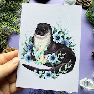 May include: A whimsical illustration of an otter holding a large, iridescent crystal surrounded by blue flowers and green leaves on a light purple background.