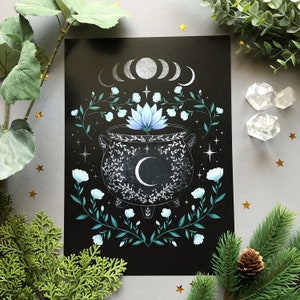 May include: A black print featuring a cauldron with a crescent moon, surrounded by floral and celestial elements. The design includes a moon phase illustration, blue flowers, and stars. The artwork has a mystical theme.