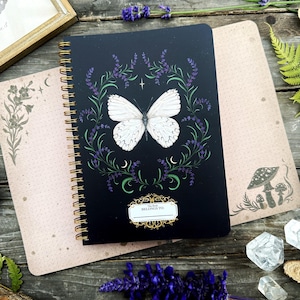 May include: A black spiral bound journal with a white butterfly and lavender flowers on the cover. The text "This Book Belongs To You" is on the cover.