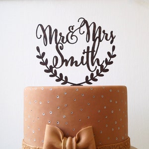 May include: A wooden cake topper with the text "Mr. & Mrs. Smith" in a cursive font, surrounded by a leafy wreath. The topper is on a brown cake with white polka dots.