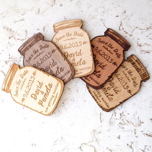May include: Six wooden save the date magnets shaped like mason jars with the text "Save the Date" and the date "9.6.2015" and the names "David & Pamela" on each magnet.