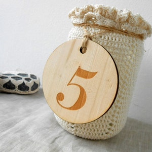 May include: A white crocheted jar with a wooden circle attached to it. The circle has the number "5" engraved on it.