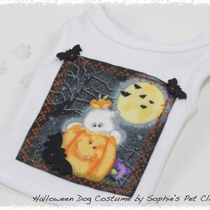 May include: White dog costume with a Halloween-themed design. The design features a cartoon ghost and a pumpkin, with a full moon and bats. The costume has black bat-shaped embellishments and the text "Halloween Dog Costume by Sophie's Pet Closet".