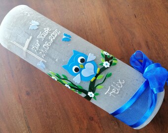 Peut inclure: Une bougie de baptême blanche avec un motif de hibou bleu, des feuilles vertes et des fleurs blanches. La bougie est décorée de paillettes argentées et du texte "Zur Taufe 21.06.2020 Felix".