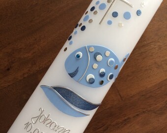May include: White baptism candle with a blue fish design, silver cross, and blue and silver dots. The candle is inscribed with the name "Johan" and the date "10.02.2019".