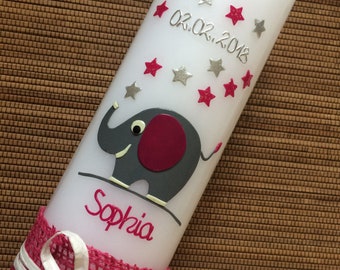 May include: White candle decorated with a gray elephant with a burgundy ear and a pink tail. The candle has red and silver stars, the date 02.02.2018, and the name "Sophia" in pink. A pink burlap ribbon with a white bow adorns the base.