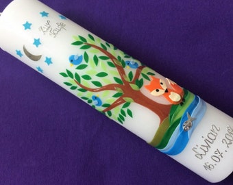 May include: White baptism candle with a blue ribbon, a tree with green leaves, blue birds, and a fox. The candle is decorated with silver stars and a crescent moon. The text "Lily Taufe" and "L'avian 16.05.2018" is written on the candle.