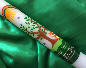 May include: White baptism candle with a rainbow, sun, butterflies, and a tree with two foxes. The candle is decorated with green leaves and a green and silver ribbon with the text "Ava Theresa 23.02.2018".