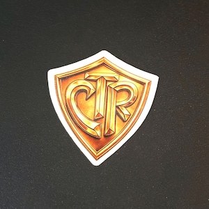 May include: A shield-shaped sticker featuring a metallic gold finish with the letters CTR embossed in the center. The design has a three-dimensional appearance with beveled edges and dark shading, outlined by a thin white border on a dark background.