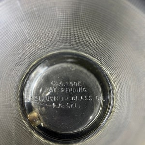 May include: Close-up of the bottom of a clear glass bowl with the text "C.A. Look Pat. Pending McLaughlin Glass Co. L.A. Cal." printed on the bottom.