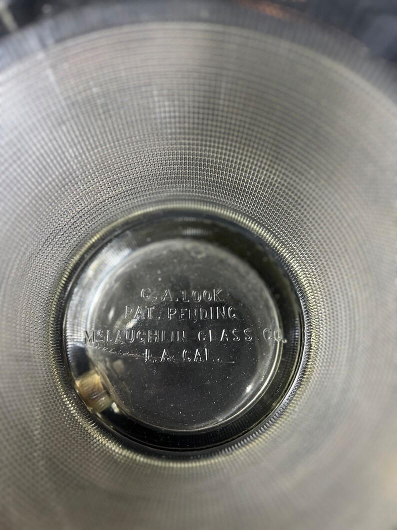 May include: Close-up of the bottom of a clear glass bowl with the text "C.A. Look Pat. Pending McLaughlin Glass Co. L.A. Cal." printed on the bottom.