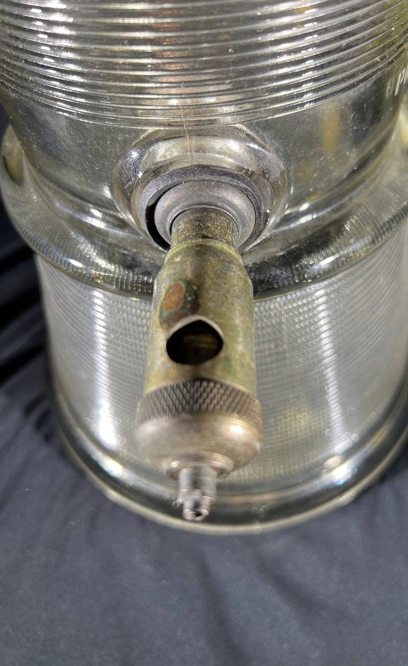 May include: Close-up of a glass bottle with a metal spout. The bottle has a textured surface and the spout has a silver finish.