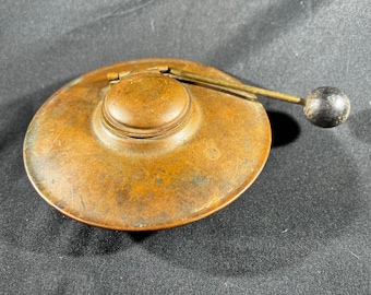 May include: A vintage copper inkwell with a lid and a wooden handle. The inkwell has a circular shape and a worn, aged patina.