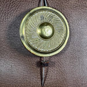 May include: A gold-toned metal pendulum with a decorative, concentric circle design. The pendulum is attached to a thin metal rod.