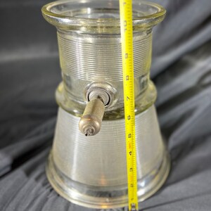 May include: A clear glass dispenser with a metal pump and a ribbed design. The dispenser is approximately 9 inches tall.