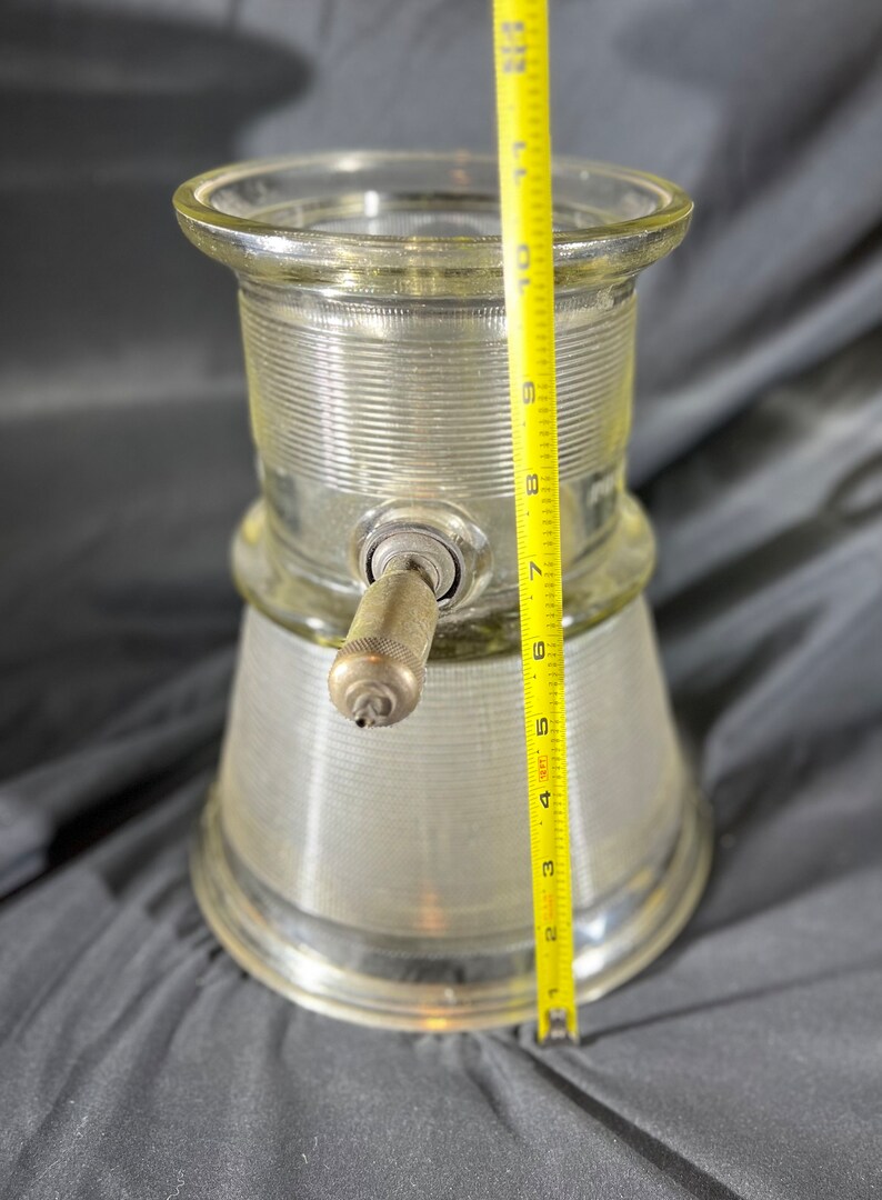 May include: A clear glass dispenser with a metal pump and a ribbed design. The dispenser is approximately 9 inches tall.